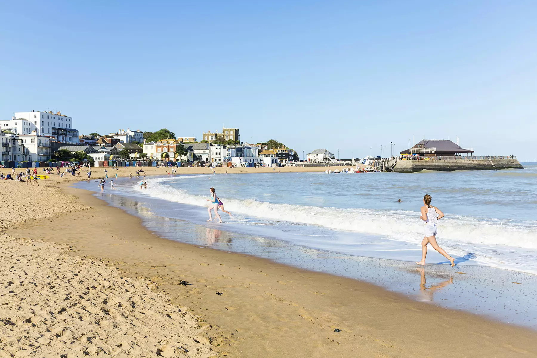 Girls running along waters edge of sandy quite beach with harbour arm in the background